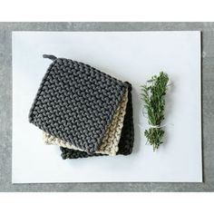 two crocheted potholders sitting on top of a cutting board next to a sprig of rosemary