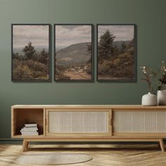 three paintings hang on the wall above a wooden cabinet in a room with green walls