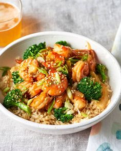 a white bowl filled with shrimp and broccoli next to a glass of beer