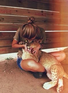 a woman is holding a small cat in her lap while sitting on the ground next to a fence