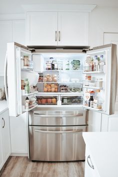 an open refrigerator filled with lots of food in a kitchen next to white cupboards