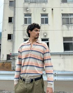 a man standing in front of a tall building wearing a striped shirt and khaki pants