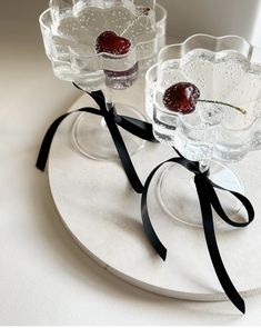 two glass dishes with cherries on them are sitting on a white plate and tied in black ribbon