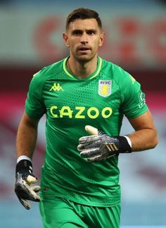 a soccer player is running with gloves on his hands and holding the ball in one hand