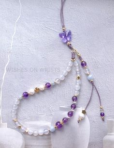 two white vases with purple and white beaded necklaces on them next to each other