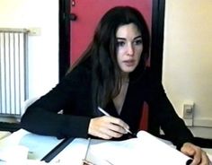 a woman sitting at a desk writing on a piece of paper with a pen in her hand