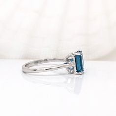 This beautiful ring features a 2.38-carat emerald cut London topaz with two earth-mined baguette diamond accents, all set in solid 14K gold. The ring exudes both elegance and durability, making it suitable for everyday wear or special occasions! This ring is made with solid 14K Gold and naturally Earth mined SI / G-H diamonds. As listed, this ring is ready to ship. If you're interested in purchasing this setting with a different center stone please message us! Emerald-cut Topaz Ring In 14k White Gold, Emerald Cut Topaz Ring In 14k White Gold, Emerald-cut Sapphire Ring With Topaz Accent Stones, Blue Topaz Baguette Cut Ring, Baguette Cut Blue Topaz Ring, London Topaz, Designer Silver Jewellery, London Blue Topaz Ring, Jewelry Showcases