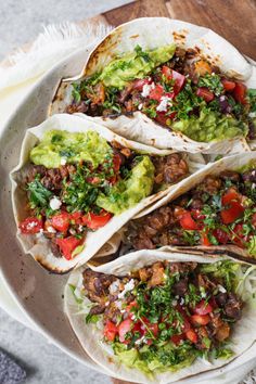 three tacos on a plate with guacamole, tomatoes and other toppings