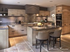 a large kitchen with wooden cabinets and marble counter tops, along with two bar stools