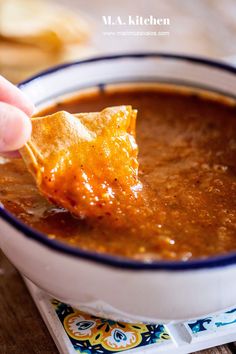 a hand holding a tortilla chip over a bowl of chili cheese quesadilla soup