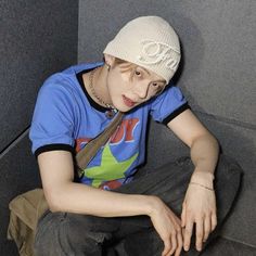 a young man wearing a hat and tie sitting on the floor in front of a wall