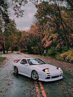 a white sports car is parked on the side of the road in front of some trees