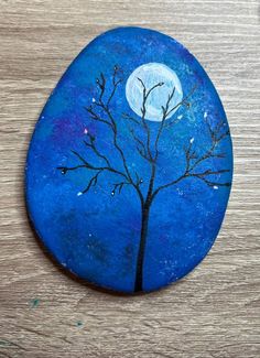 a painted rock with a tree and moon in the background on a wooden table top