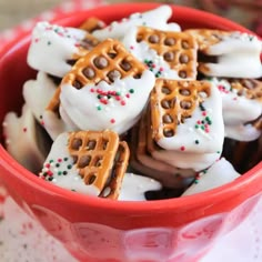 chocolate dipped pretzel sandwiches in a red bowl with white frosting and sprinkles