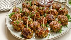 meatballs with toothpicks on a plate next to dipping sauce and breadcrumbs