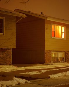 a house with snow on the ground in front of it and two windows lit up at night