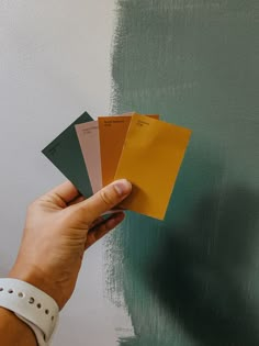 a person holding some paint samples in their hand next to a wall with green and yellow colors