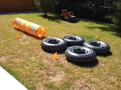 four tires are laying on the ground in front of an orange tube and yellow cones