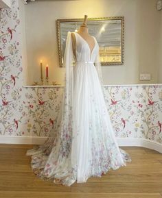 a white wedding dress on display in front of a wallpapered room with candles