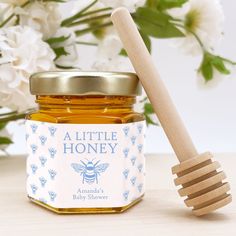 a jar of honey with a wooden spoon next to it and flowers in the background