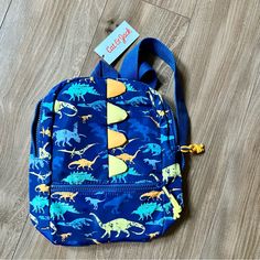 a blue backpack with dinosaurs on it sitting on a wooden floor next to a tag