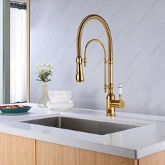 a kitchen sink with gold faucet and marble counter top next to a window