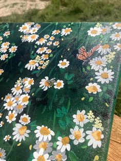 a close up of a table with flowers and butterflies painted on the top, along with grass in the background