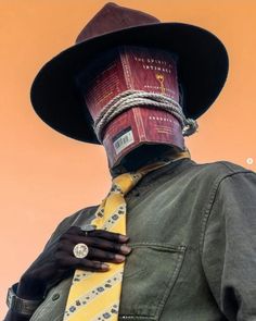 a man wearing a hat and tie with a book on his head, standing in front of an orange sky