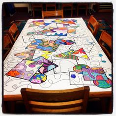 a long table covered with colorful paper cut outs and wooden chairs in front of it