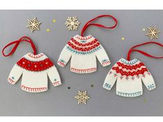 two knitted sweaters and snowflakes are hanging from red ribbon on a gray background