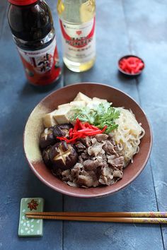 a bowl filled with meat and vegetables next to chopsticks on top of a table