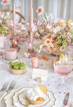 the table is set with pink and white flowers, silverware, candles, and napkins