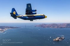 a blue and yellow plane flying over the ocean with a boat in the water behind it