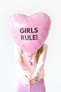 a woman holding a pink heart shaped balloon with the words girls rules written on it