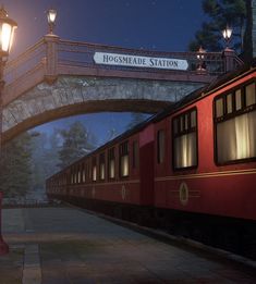 a red train passing under a bridge at night with street lamps on either side and a sign that reads hodsmeade station above it