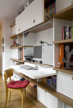 a desk with two computers on top of it and some bookshelves in the background