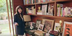 a woman standing next to a book shelf filled with books