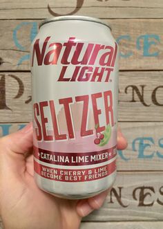 a hand holding a can of seltzer on top of a wooden table next to a wall