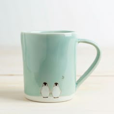 two small penguins are sitting on a light green coffee mug with white trim and black eyes