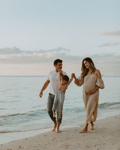 a family walking on the beach holding hands and laughing at each other as they walk towards the water