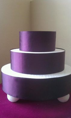 a three tiered cake sitting on top of a purple table cloth covered floor next to a white wall