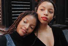 two women standing next to each other in front of a building with black shutters