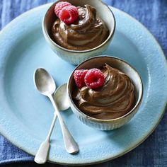 two small cups filled with chocolate pudding and raspberries on a blue plate next to a spoon