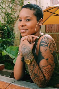 a woman with tattoos and piercings on her arm sitting in front of an umbrella