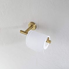 a roll of toilet paper is hanging on the wall next to a gold toilet brush