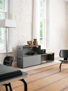 a living room filled with furniture next to a large white brick wall and two windows