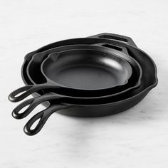 three black cast iron skillets stacked on top of each other, one with handles