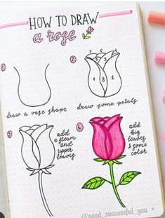 an open notebook with some drawings and markers on the pages, including a pink rose