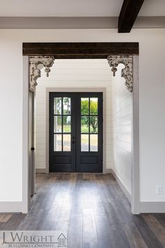 an empty room with two black doors and wood floors in front of the door is a white painted wall