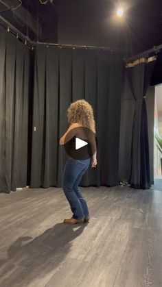 a woman standing on top of a wooden floor in front of a black curtained wall